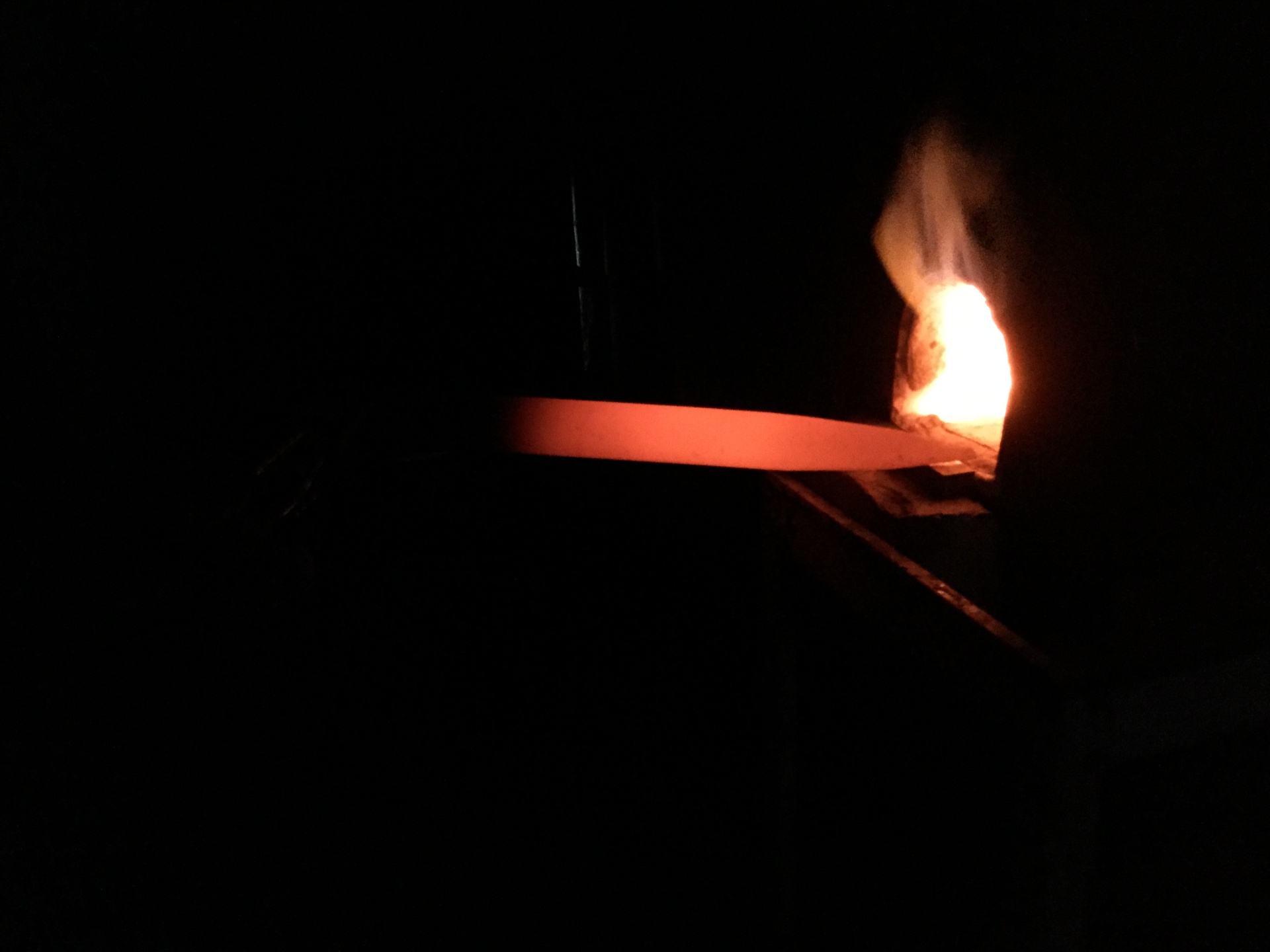 Glowing hot steel bar pulled from the forge in the dark