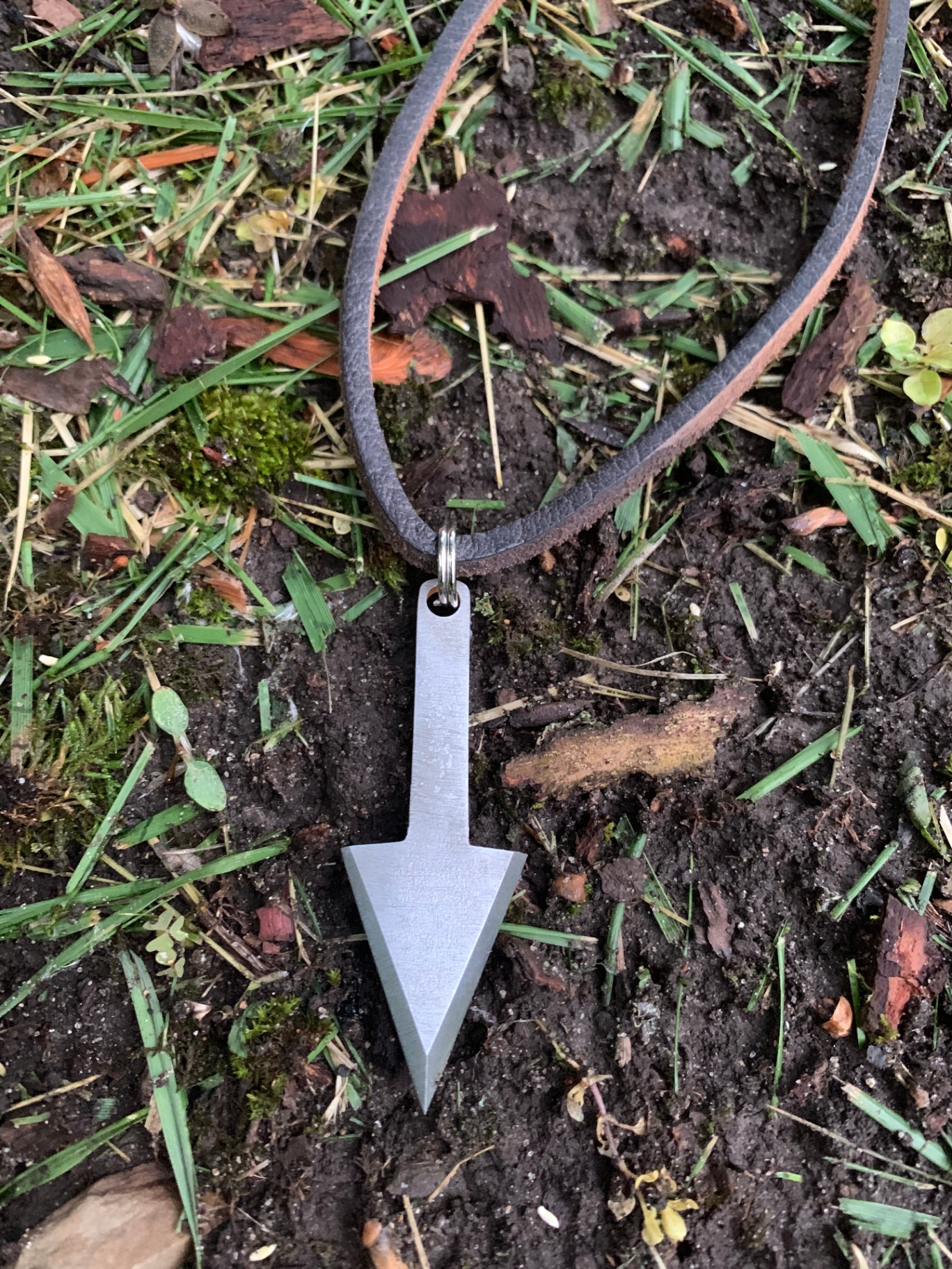 Hand-ground arrowhead pendant on a leather cord in the grass
