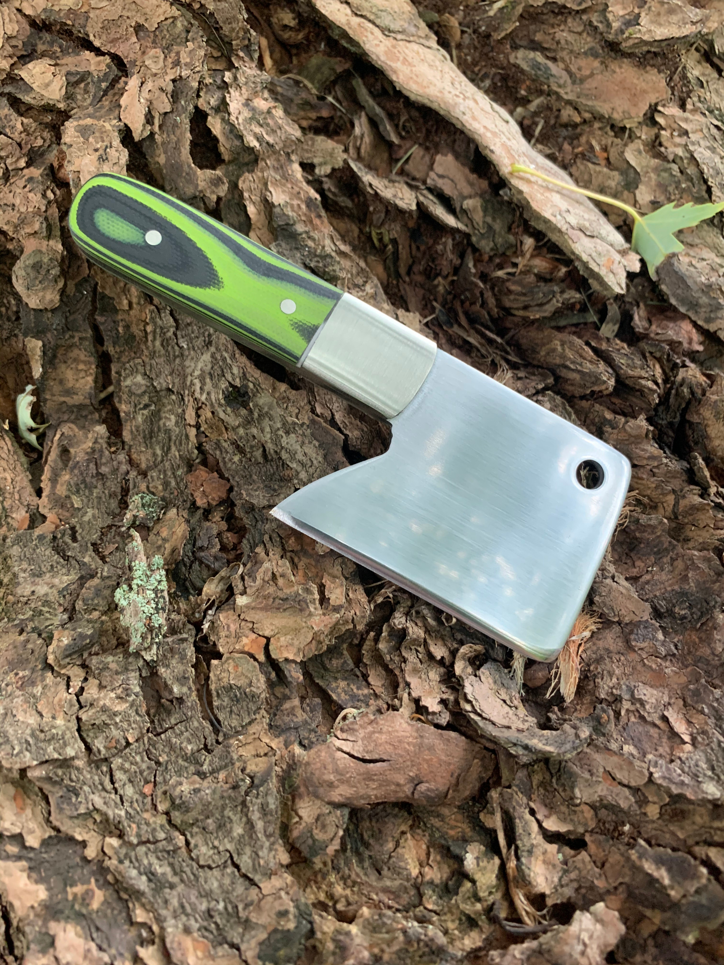 Mini cleaver with green and black G10 handle on tree bark