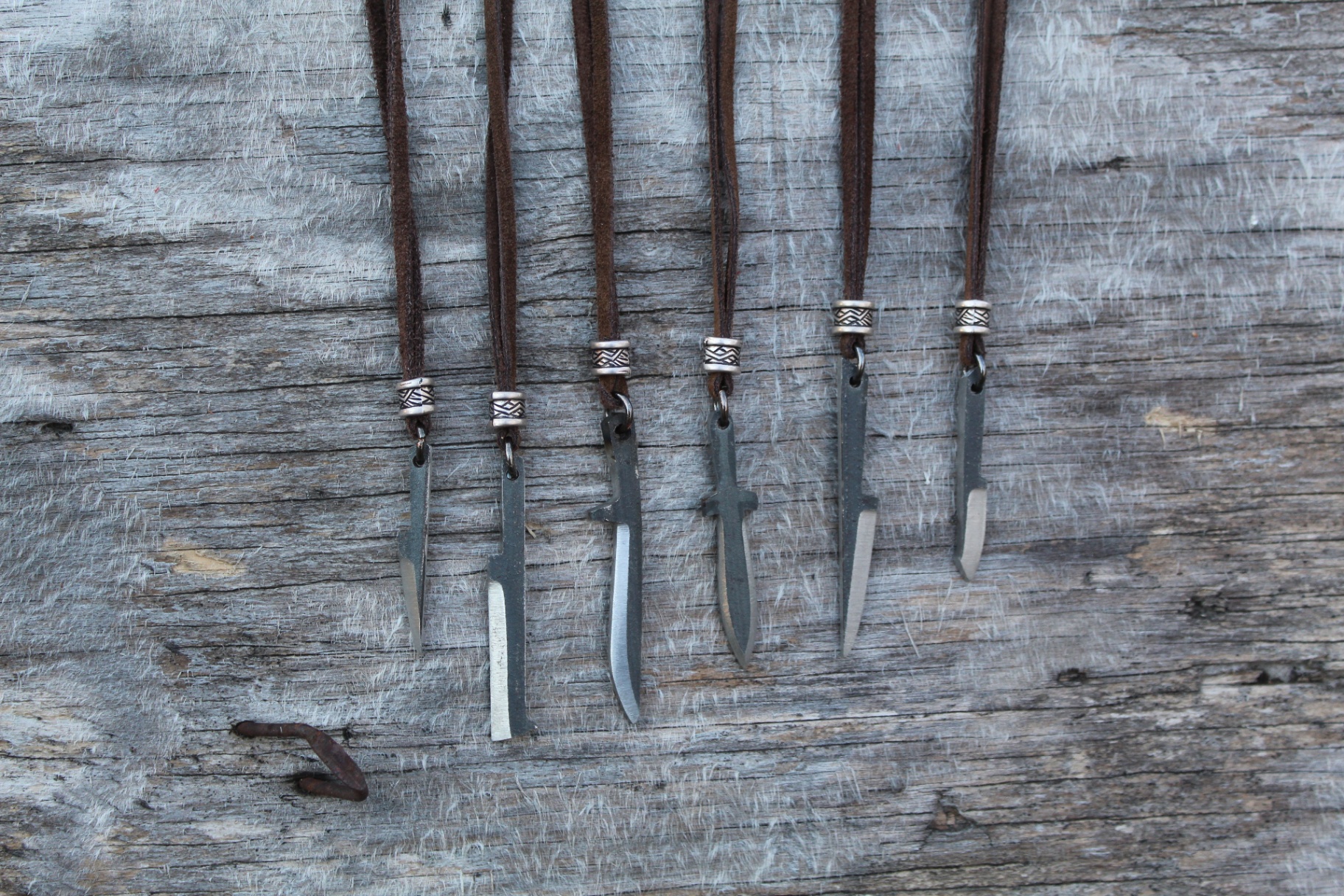 Six handmade pendants hanging on leather cords against a weathered board