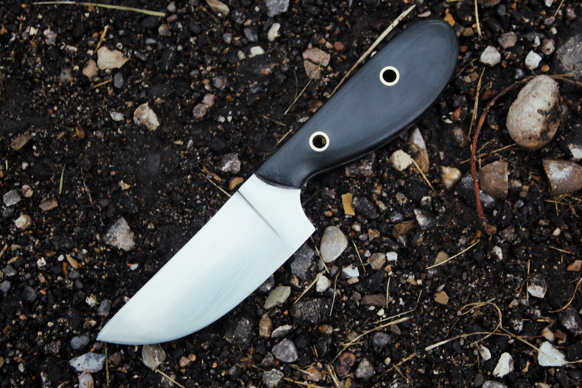 Custom-designed knife with black G10 handle on gravel and earth