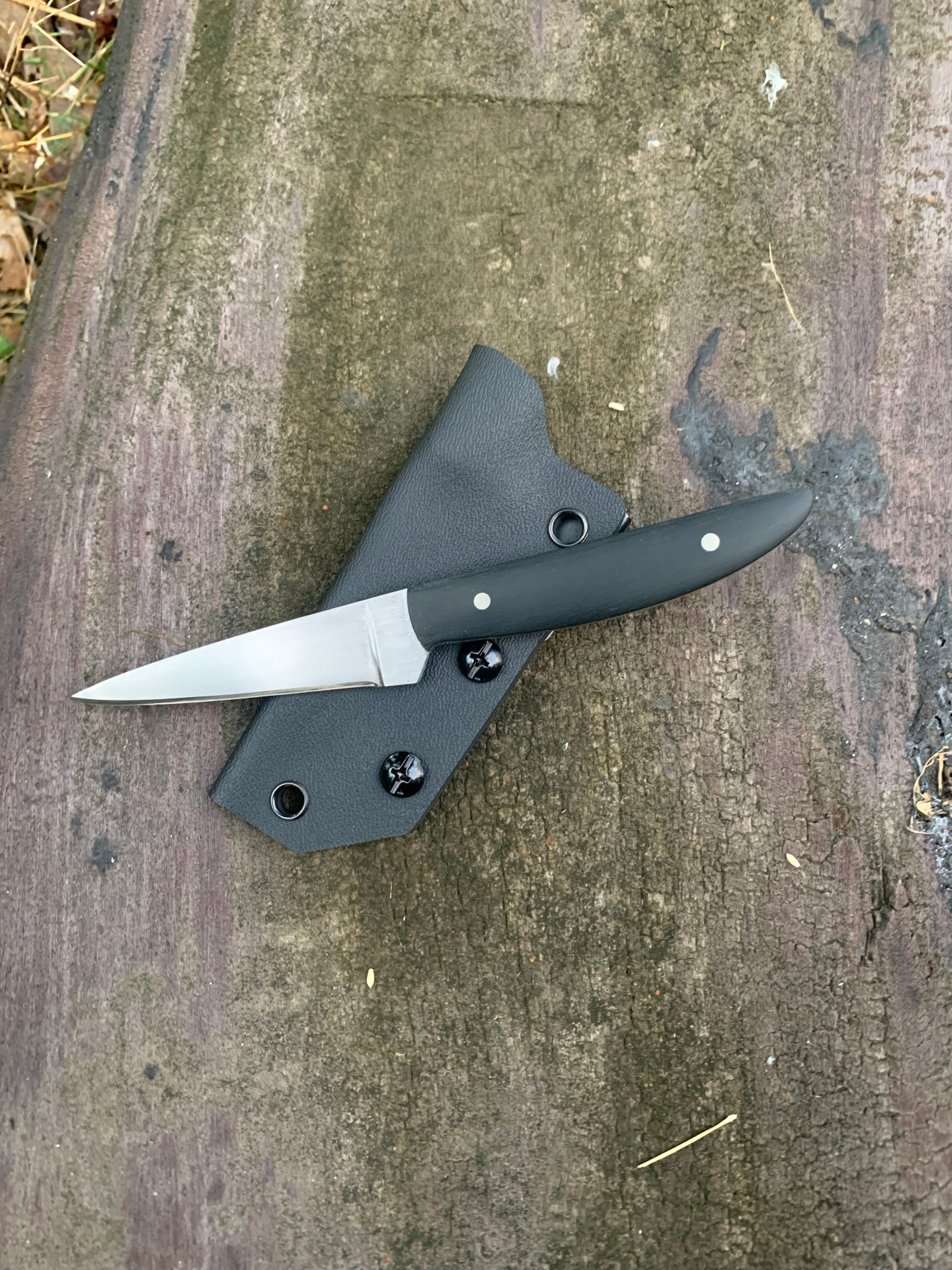 EDC knife with black handle and kydex sheath on weathered wood