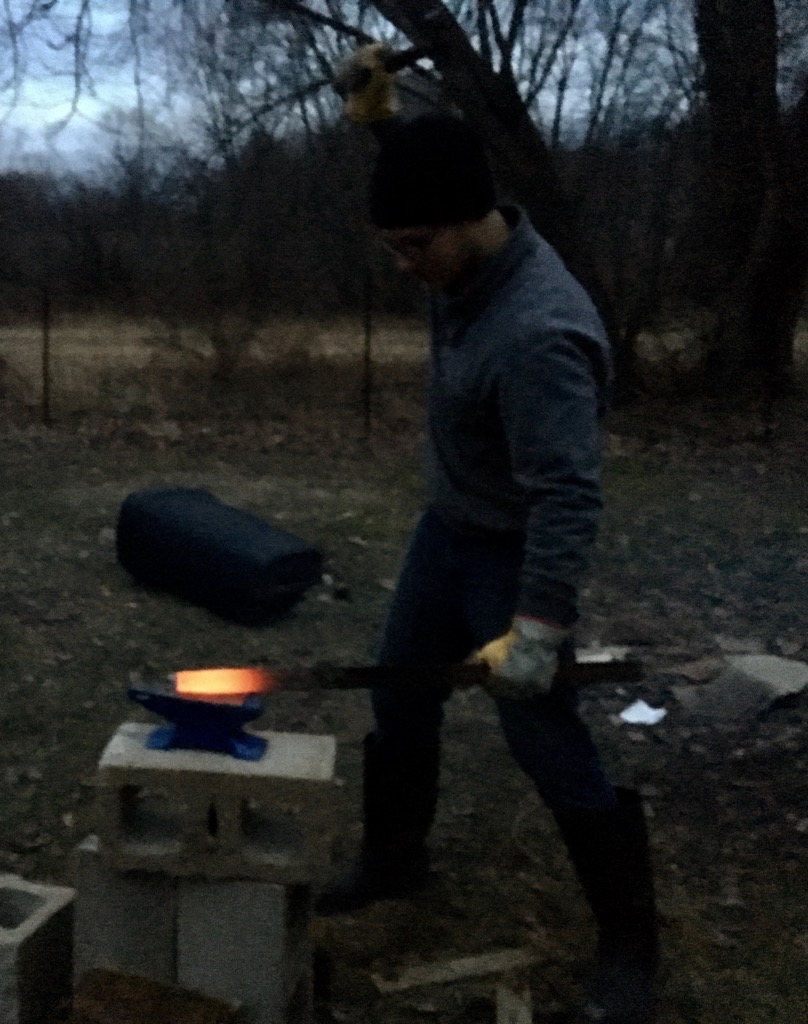 Hunter forging a glowing hot blade on the anvil at dusk