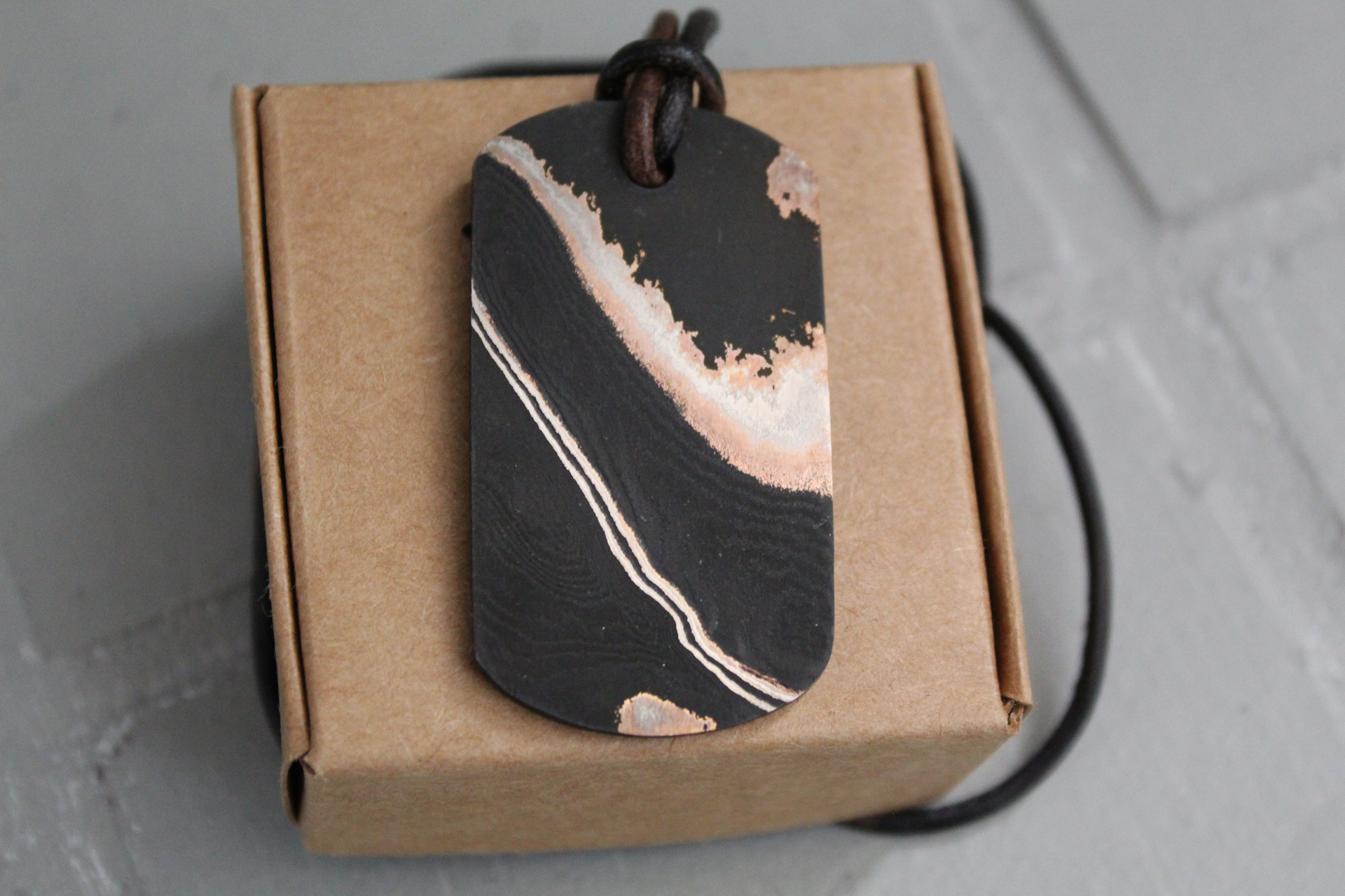Damascus dog tag pendant with copper accents on a Big H branded box