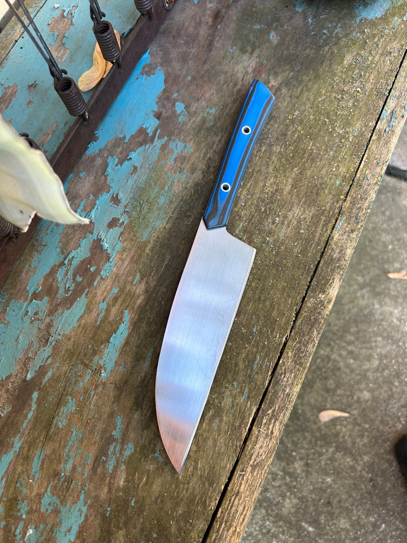 Kitchen knife with blue G10 handle on weathered blue bench