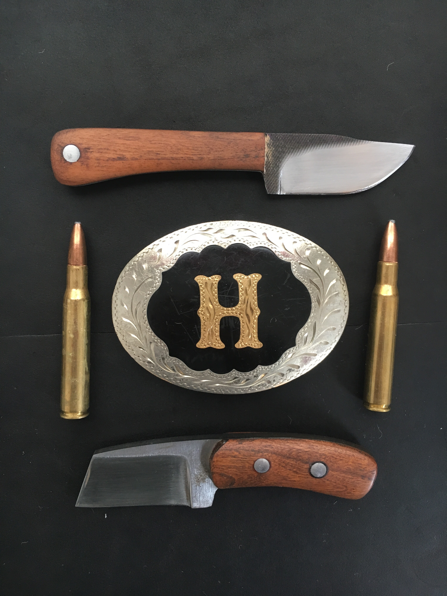 Two wood-handled knives arranged around the Big H belt buckle with rifle cartridges