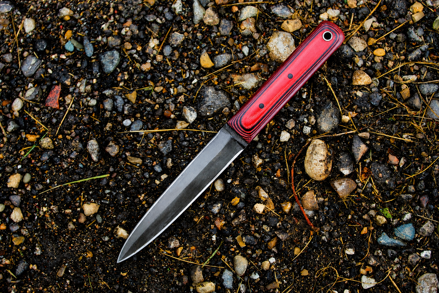 Dagger with red micarta handle on wet gravel